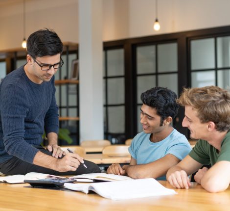 Serious teacher checking assignment of two students. Serious man in glasses pointing pen at notes of two cheerful guys. Education and internship concept
