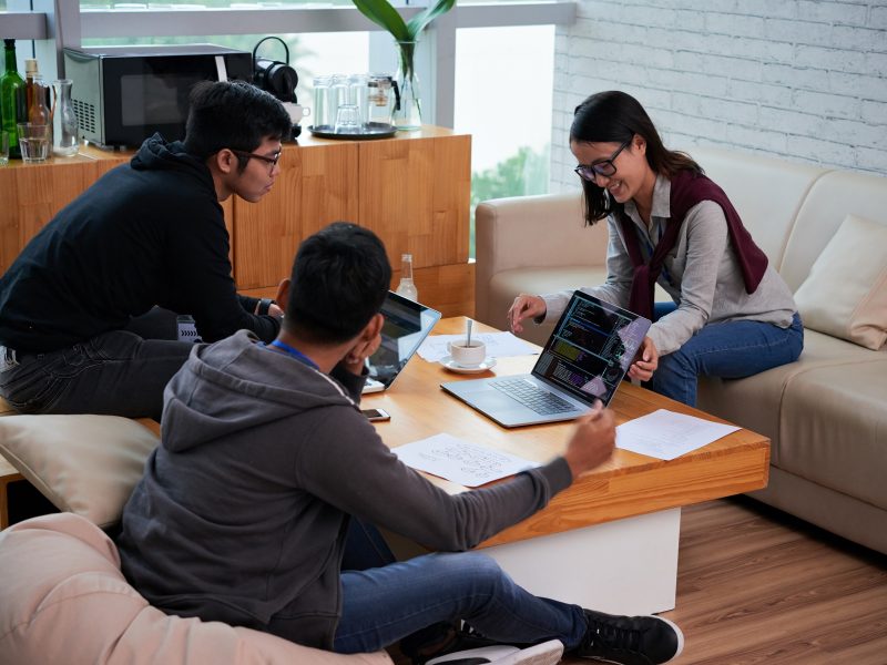 Smiling young female programmer showing her programming code to coworkers